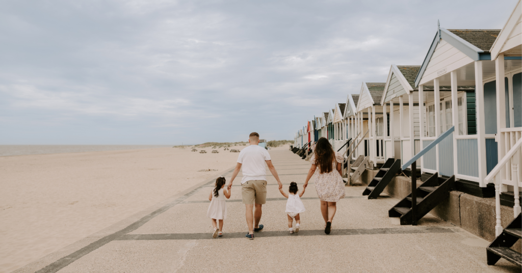 Family walking along seafront with beach huts let by Durrants Holiday Cottages, Southwold